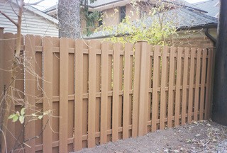 This is an image of a board on board fence. This is a tall partially-open fence with vertical boards alternatelty attached to opposite sides of the horizontal supports.