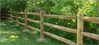 Image of a split rail fence. This fence has horizontal rails that are roughly-hewn and spaced two to three feet apart.